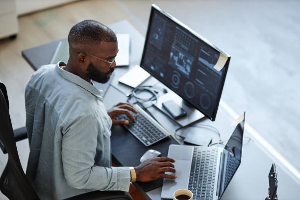 A focused man working at a desk with multiple screens and devices, demonstrating a high-tech and data-driven work environment.