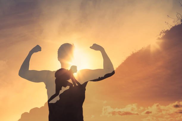 Silhouette of a strong man flexing muscles with a double exposure of a man climbing a mountain at sunrise, symbolizing mental toughness and perseverance.
