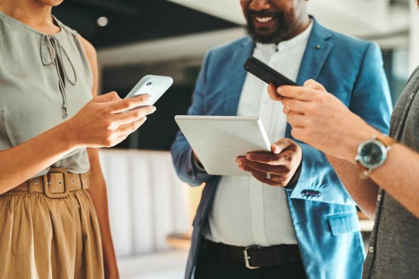 A group of professionals collaborating in a modern office, holding smartphones and a tablet, smiling and engaged in discussion, showcasing productivity and teamwork.