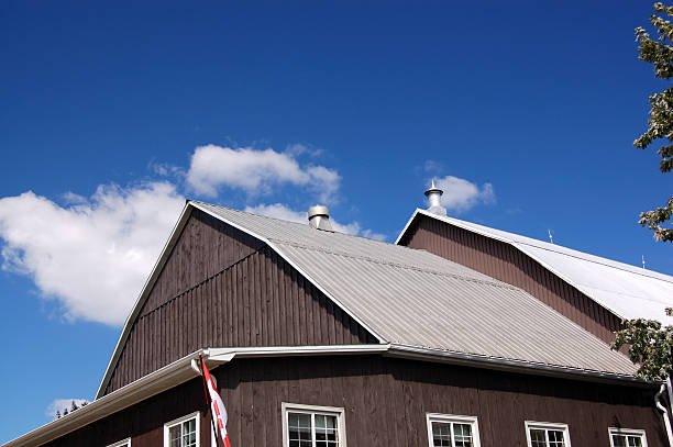 A barndominium with a dark wooden exterior and metal roof under a clear blue sky with a flag, showcasing rustic bachelor pad design.