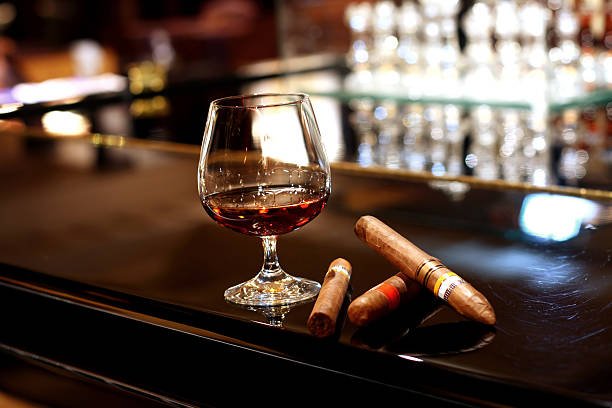 A Gen Z man in a suit lighting a cigar at a cigar lounge with leather chairs and dim lighting, showcasing cigar lounges for Gen Z.
