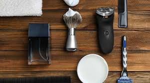 A grooming kit with a razor, electric trimmer, shaving brush, cologne, towel, and other tools on a wooden surface, symbolizing men's grooming upgrades.