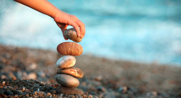 A hand balancing a stone on a stack of rocks by the sea, symbolizing quiet ambition and balance.