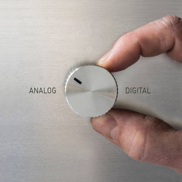 A hand turning a dial from "Digital" to "Analog" on a metallic surface, symbolizing a switch to analog technology.
