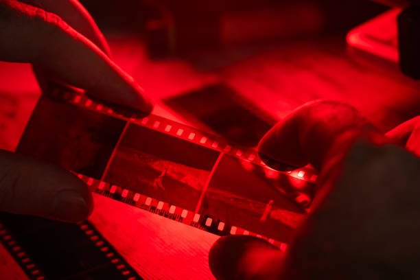 Image of hands holding and examining a strip of analog film under red light, symbolizing manual photography skills, alongside the title "Analog Mastery: 7 Unstoppable Manual Skills Every Digital Man Must Relearn in 2025."