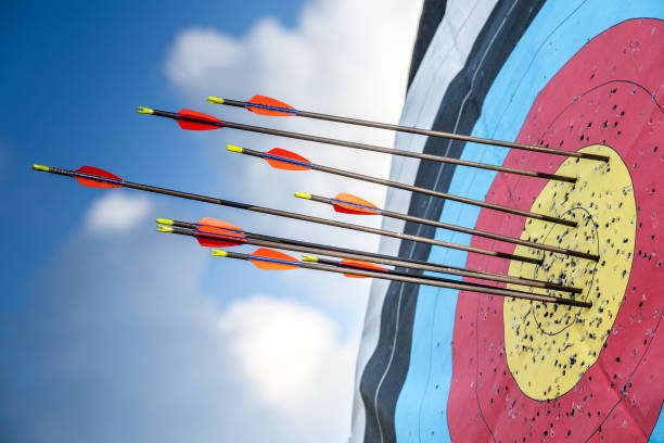 A close-up image of a target with multiple arrows embedded, set against a clear blue sky with some clouds, symbolizing the focus and precision of archery beginners.