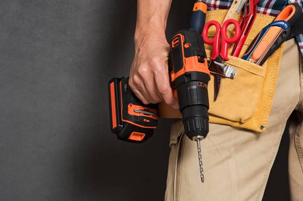 A man holding a cordless drill with a tool belt filled with scissors, pliers, and other tools, symbolizing hands-on DIY gear for men.