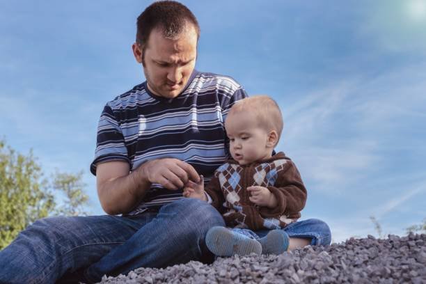 Image of a father sitting with his young son on a rocky surface under a clear blue sky, symbolizing grit-based parenting, alongside the title "Grit-Based Parenting: 7 Proven Ways Modern Dads Are Raising Resilient Sons in 2025."