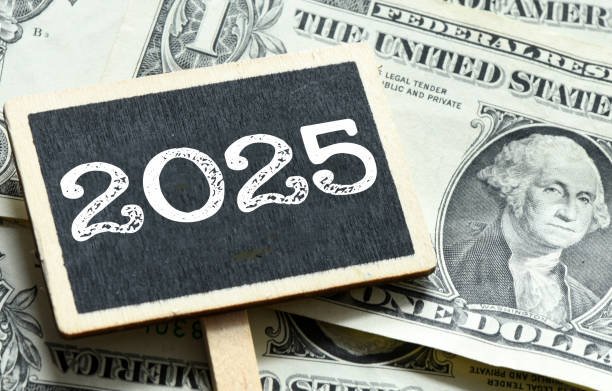 A black sign with "2025" written on it placed over a pile of U.S. one-dollar bills, symbolizing high paying opportunities in 2025.