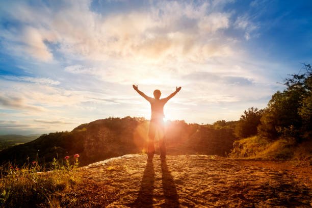 Man standing on a mountain cliff at sunrise with arms raised, embracing nature and inner stillness—symbolizing masculine spirituality and personal strength