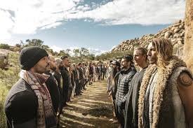 Image of a group of rugged men standing in a line on a rocky, outdoor terrain under a clear sky, symbolizing wild masculinity, alongside the title "Wild Masculinity: 7 Mythology Archetypes Men Are Reclaiming to Forge Modern Identity in 2025."
