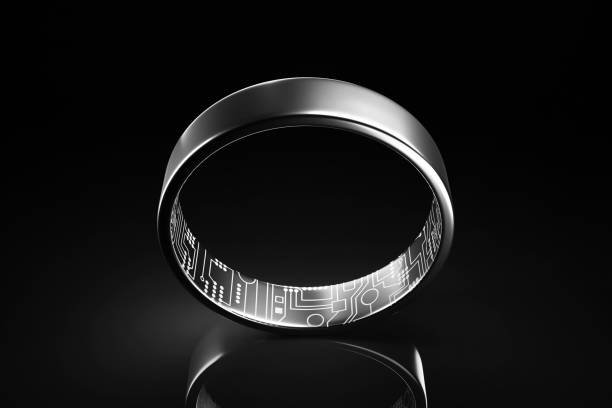 A sleek, dark metallic fitness ring, showcasing its high-tech design with an illuminated circuit board pattern visible on the inner band, set against a solid black background.