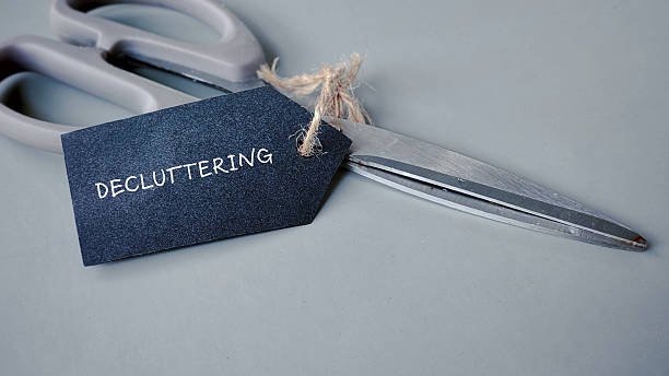 A black tag with the word "DECLUTTERING" written on it, tied with twine to a pair of scissors, symbolizing the concept of using tools to cut out clutter.