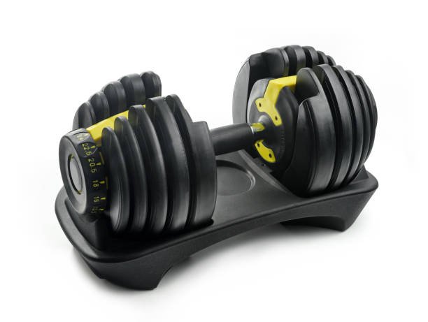 A modern, black and yellow adjustable dumbbell shown resting in its storage cradle against a clean white background.