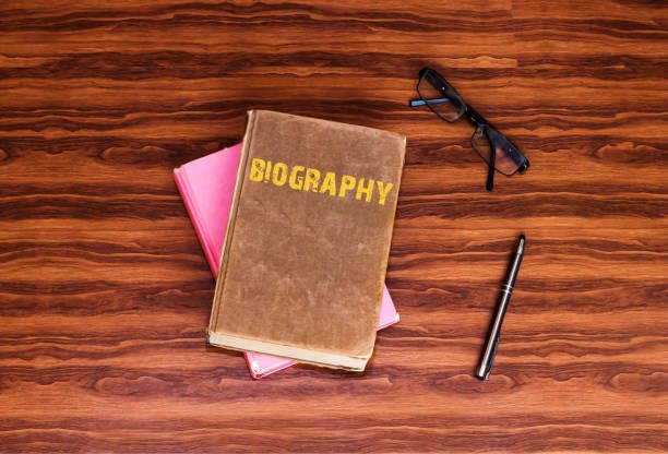 Top 5 Biographical Books: Unleash Your Potential with These 5 Monumental Life Stories Old biographical book titled "BIOGRAPHY" stacked on a pink book, next to black reading glasses and a pen on a dark wooden desk.